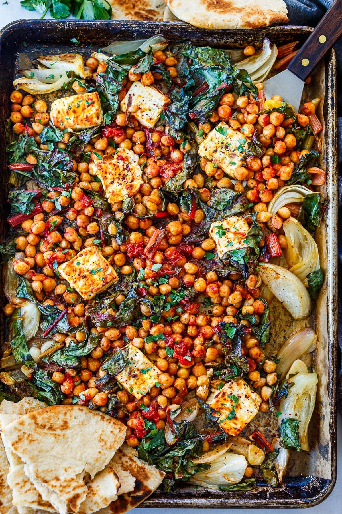 sheet pan with baked feta with chickpeas in harissa sauce, onions, chard, and naan.