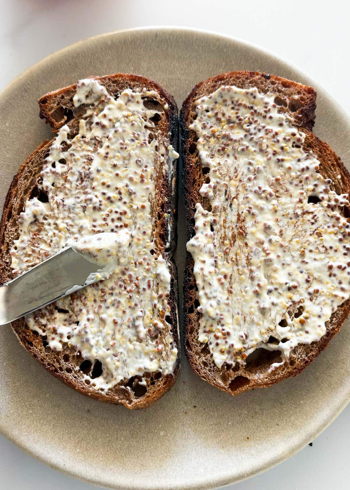 knife spreading mayonnaise and whole grain mustard mixture on toasted sourdough.