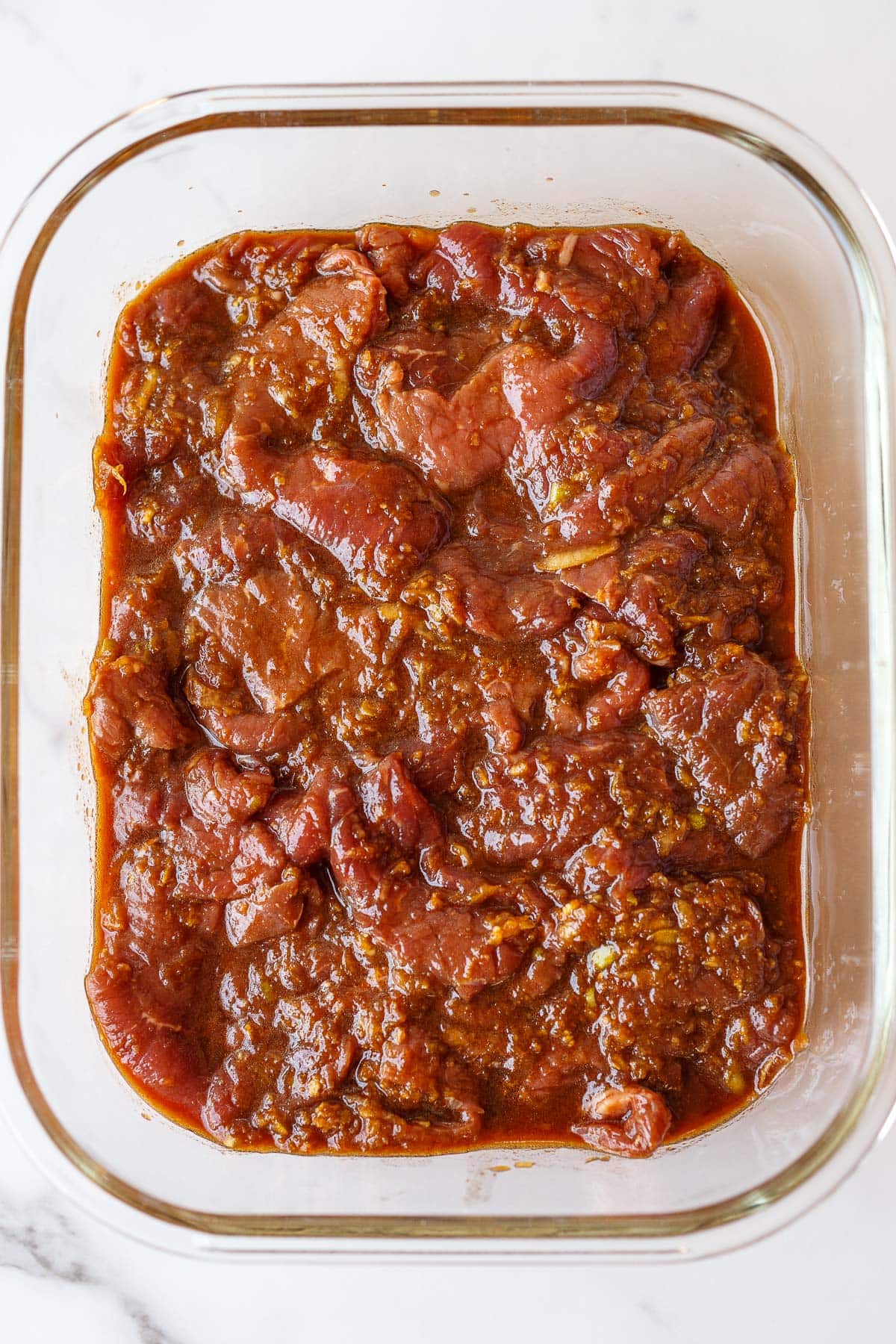 beef marinating in Korean marinade in glass rectangular dish. 