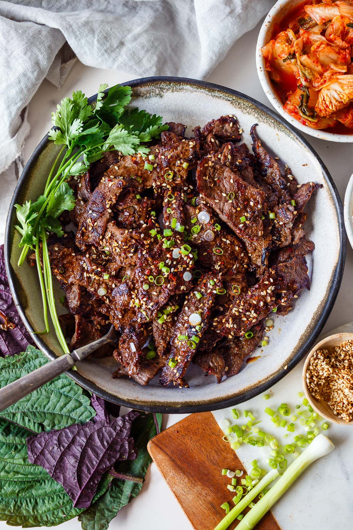 Korean bulgogi beef on plate with fresh cilantro, garnished with sesame seeds and green onions. 