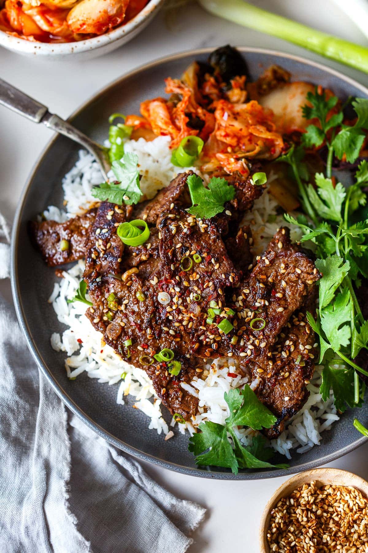 beef bulgogi on rice with kimchi and cilantro, garnished with sesame seeds, chili flakes, and green onions. 