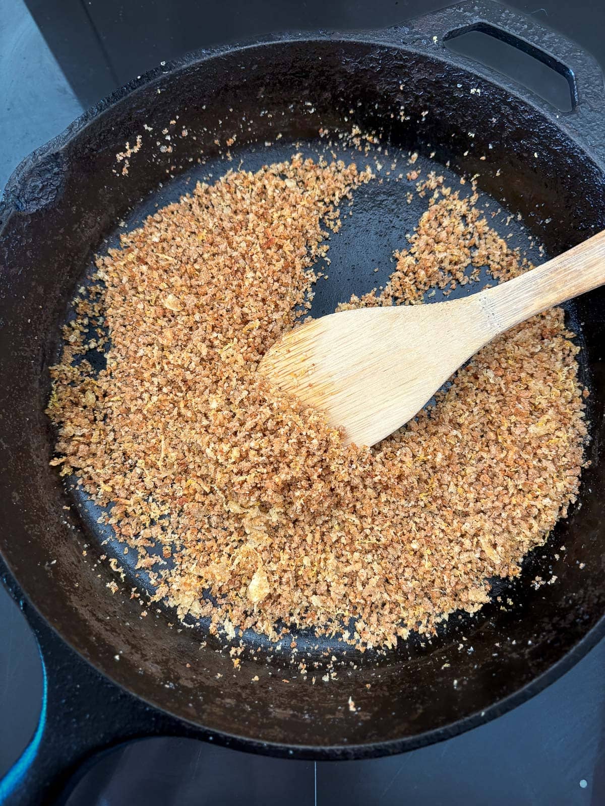 wood spoon stirring panko in cast iron skillet. 