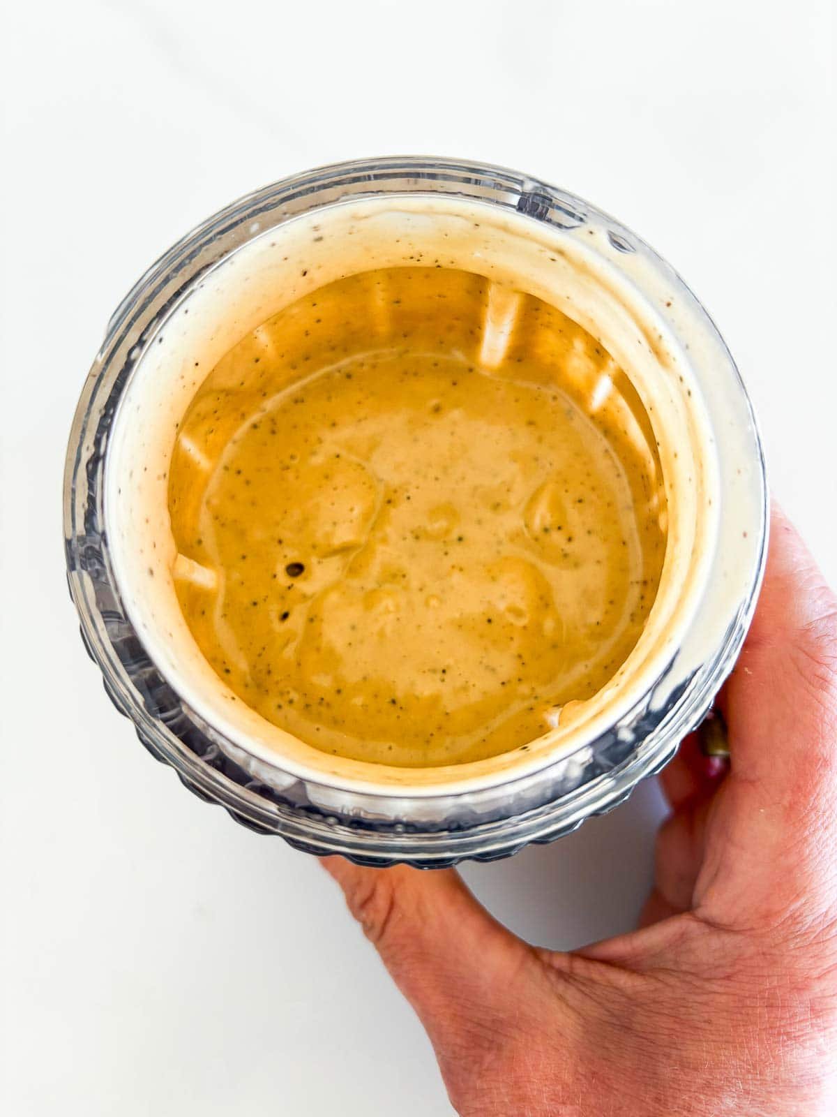 blended caesar dressing in glass jar with hand holding it. 