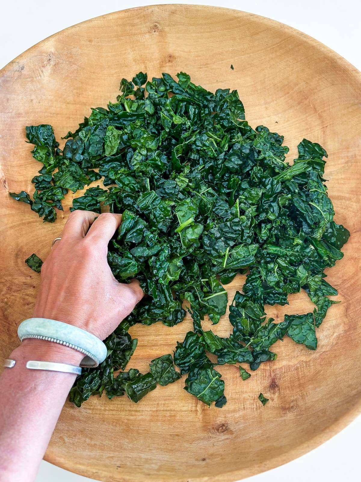 hand massaging kale in large wood bowl. 