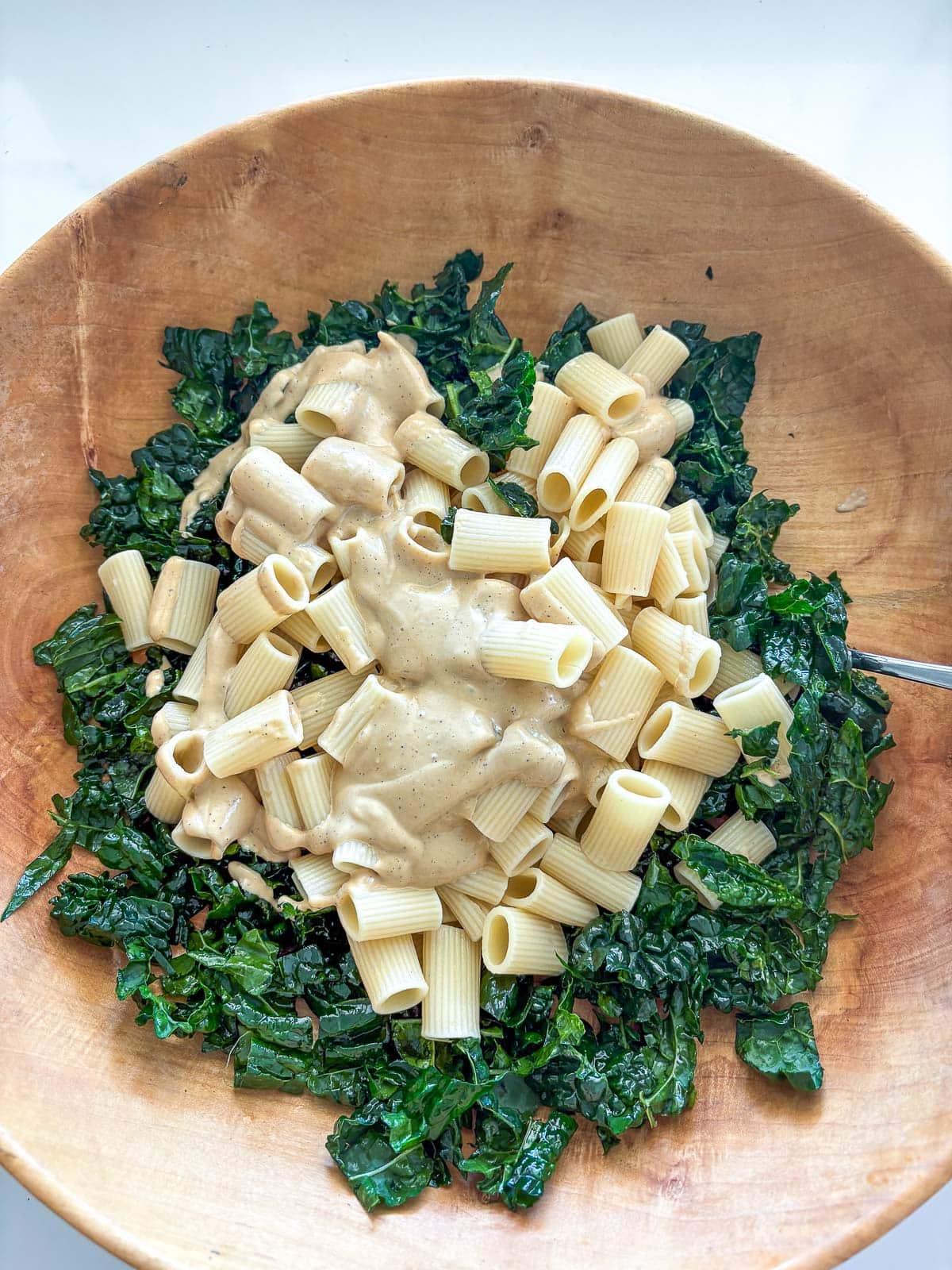 large wood bowl with kale, pasta, and caesar dressing.