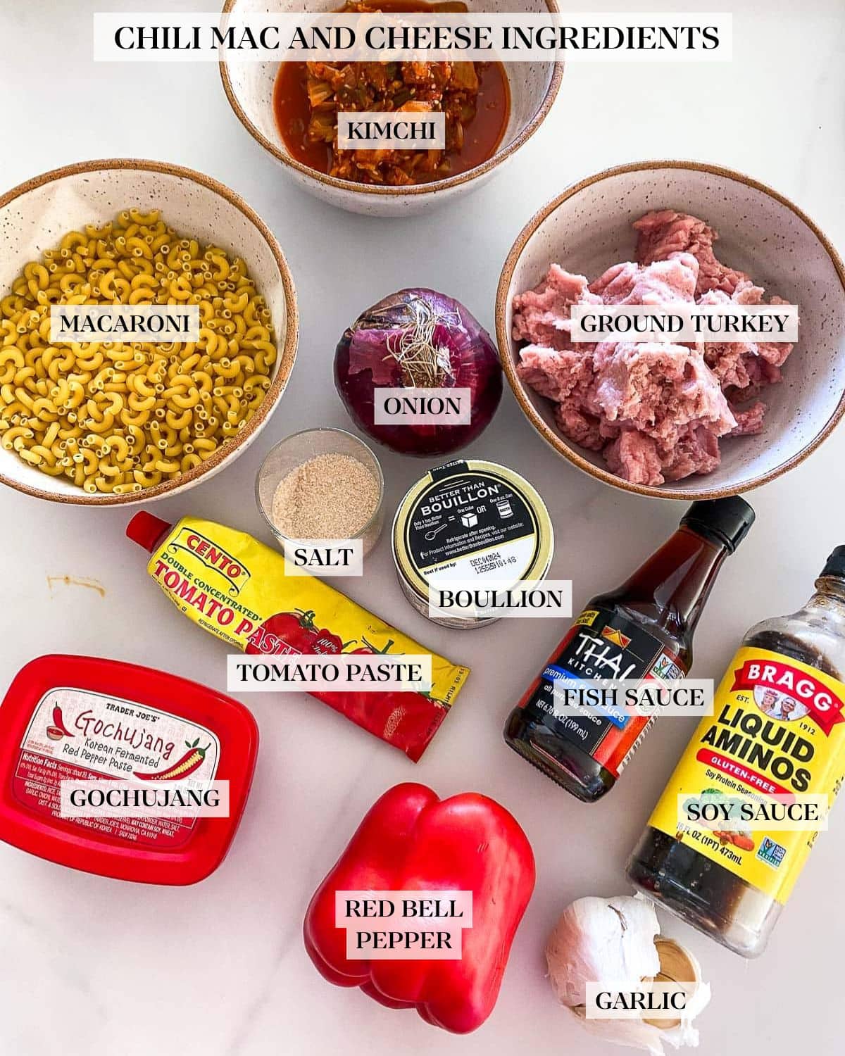 ingredients organized for kimchi chili mac and cheese - bowls of kimchi, macaroni, ground turkey, and red onion, sugar, bouillon, tomato paste, fish sauce, liquid aminos, gochujang, red bell pepper, garlic.