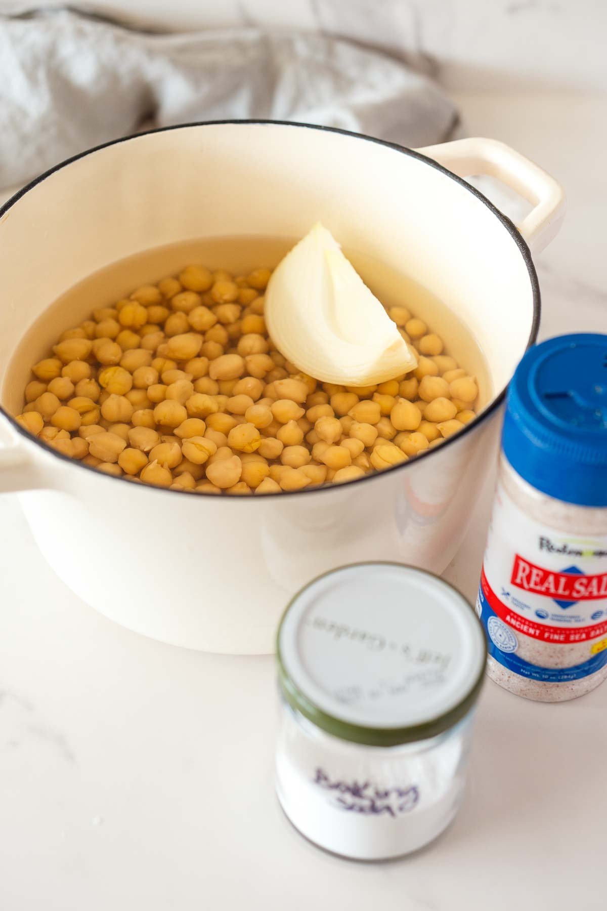 dutch oven with soaked chickpeas in water with onion wedge - salt and baking soda in front of the pot.
