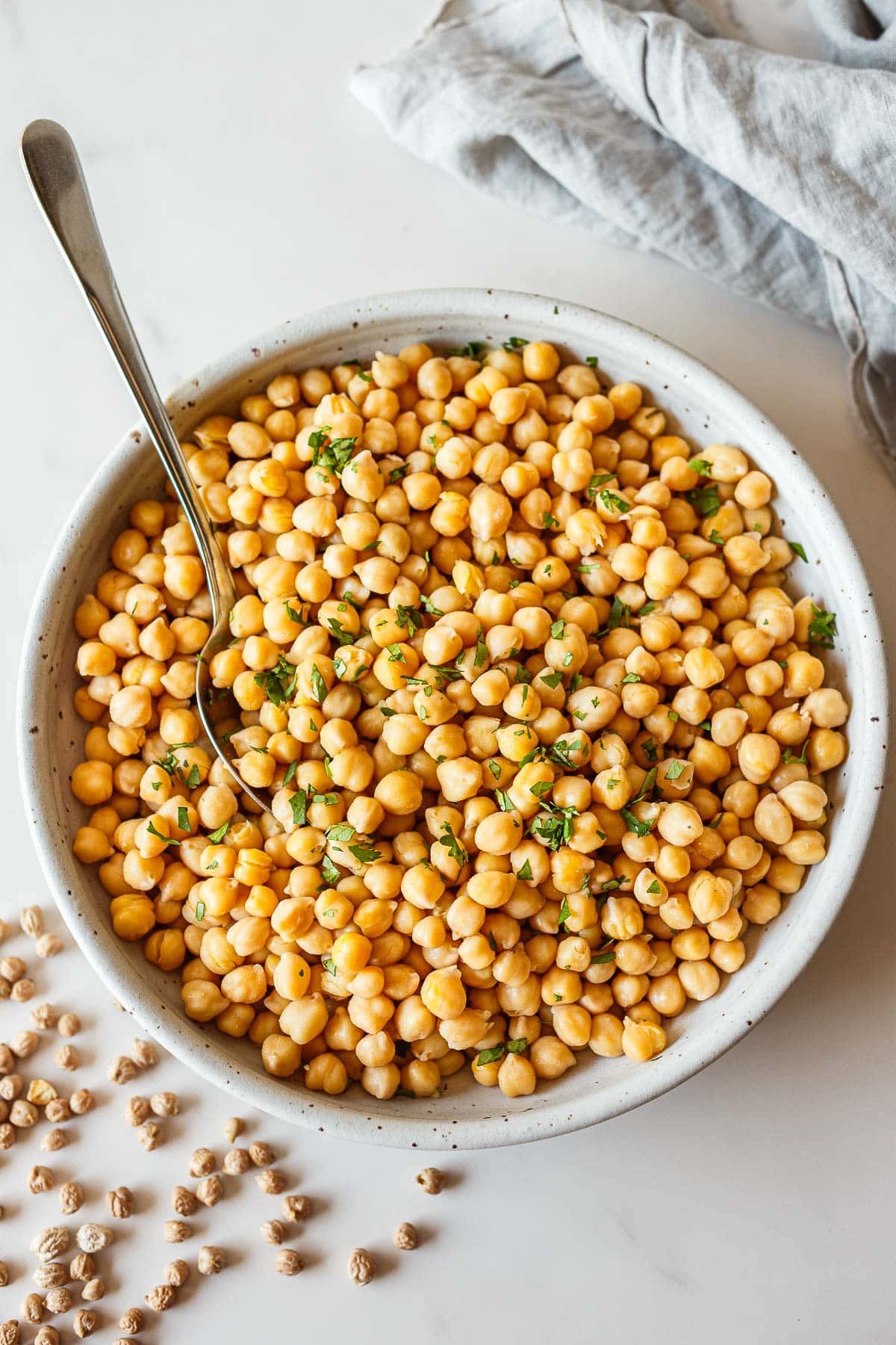 ceramic dish with cooked chickpeas garnished with parsley with spoon.