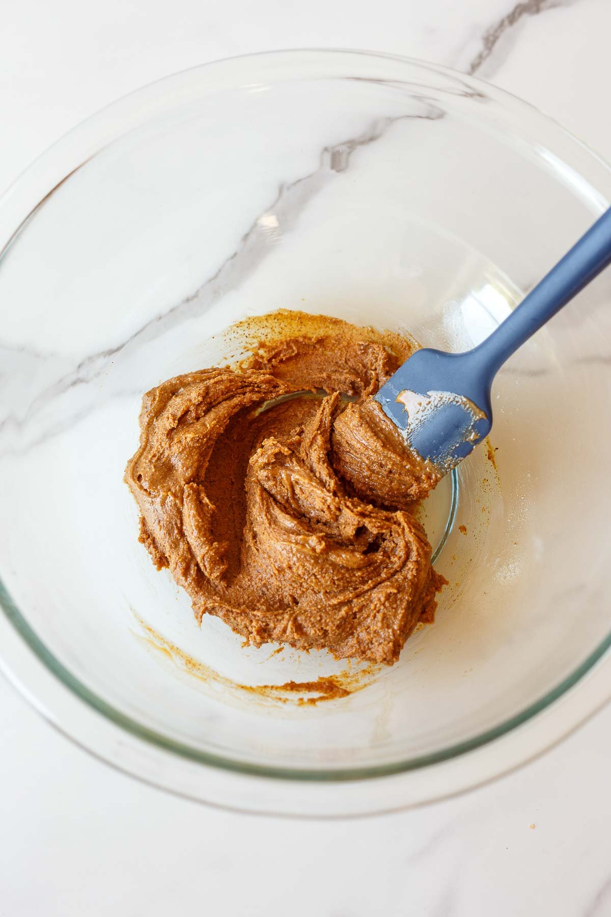 glass mixing bowl with almond butter, salt, and vanilla mixed together with silicone spatula. 