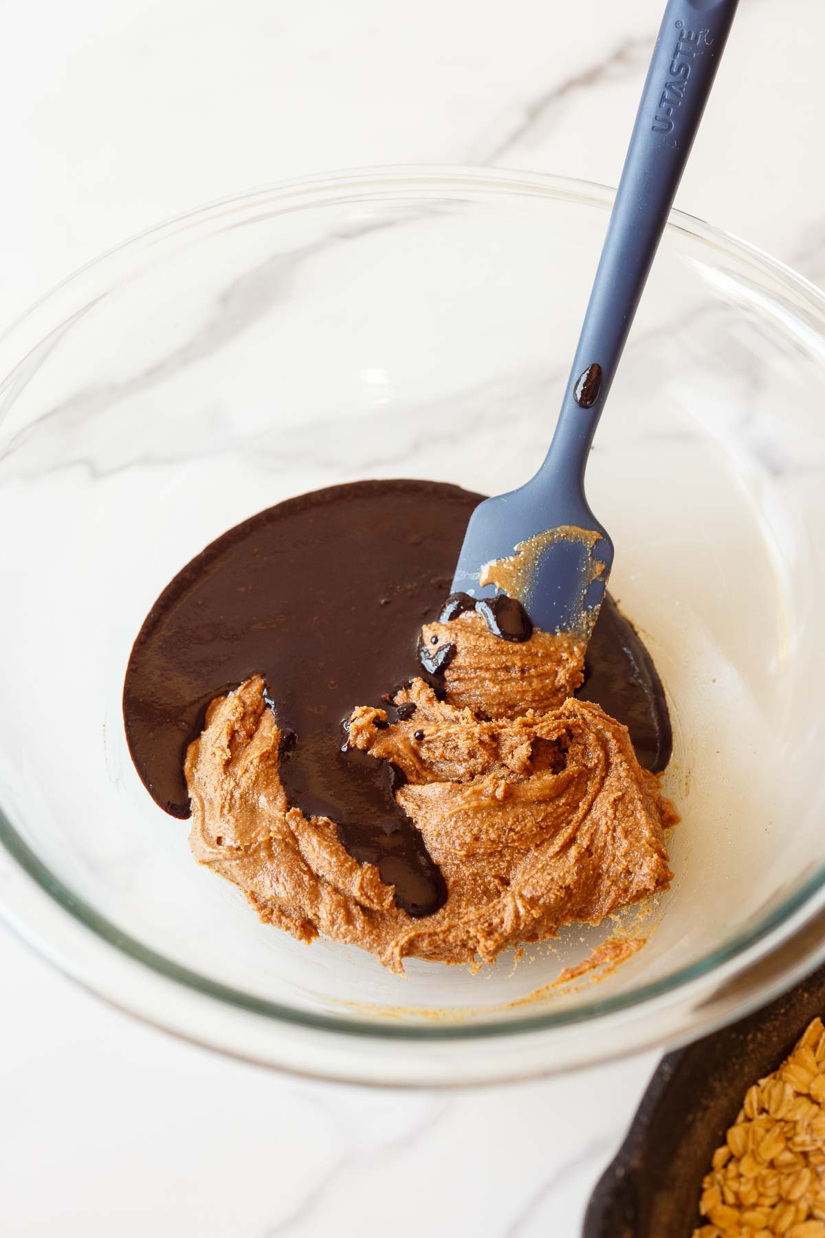 glass mixing bowl with melted chocolate mixture poured into almond butter mixture with silicone spatula. 