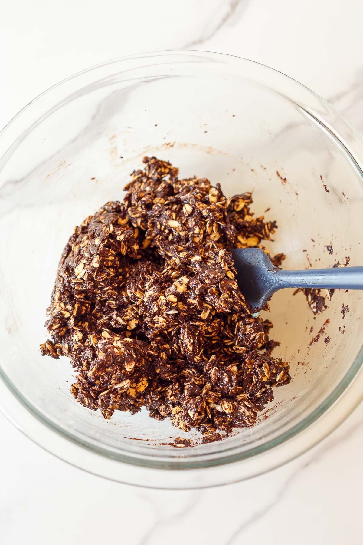 glass mixing bowl with silicone spatula mixing together the no bake cookies mixture. 