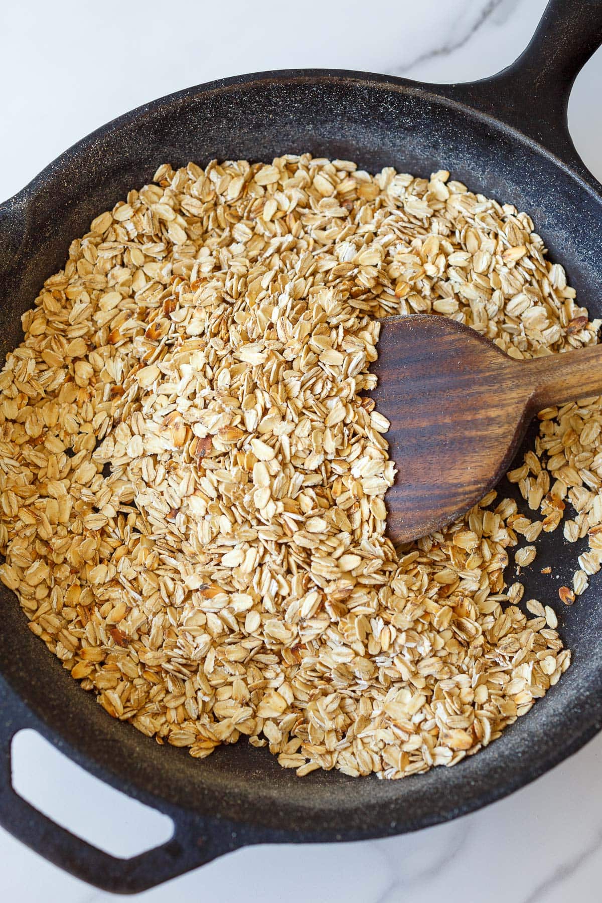 cast iron skillet toasting oats with a wooden spatula. 