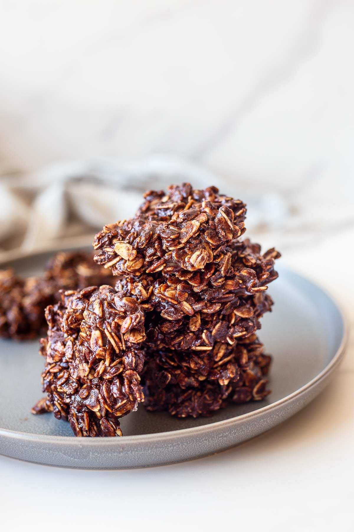 plate with a stack of chocolate no bake cookies with one cookie leaning against the side. 