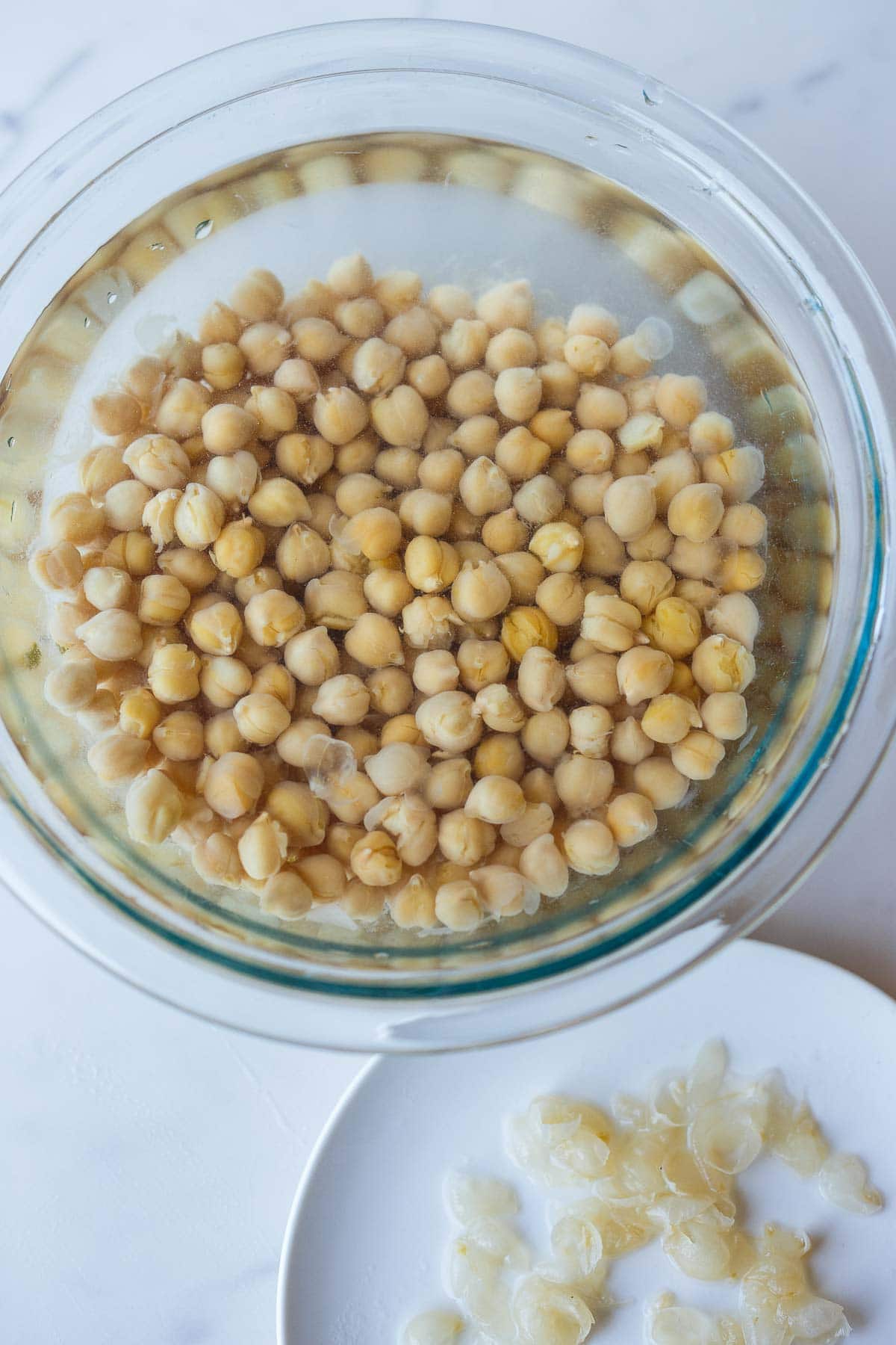 glass mixing bowl with chickpeas next to plate with skins removed. 