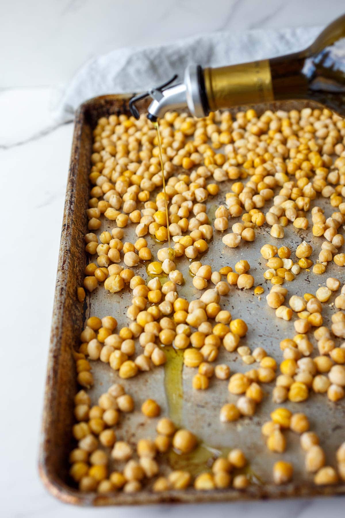 olive oil drizzled over top of baking sheet with chickpeas.