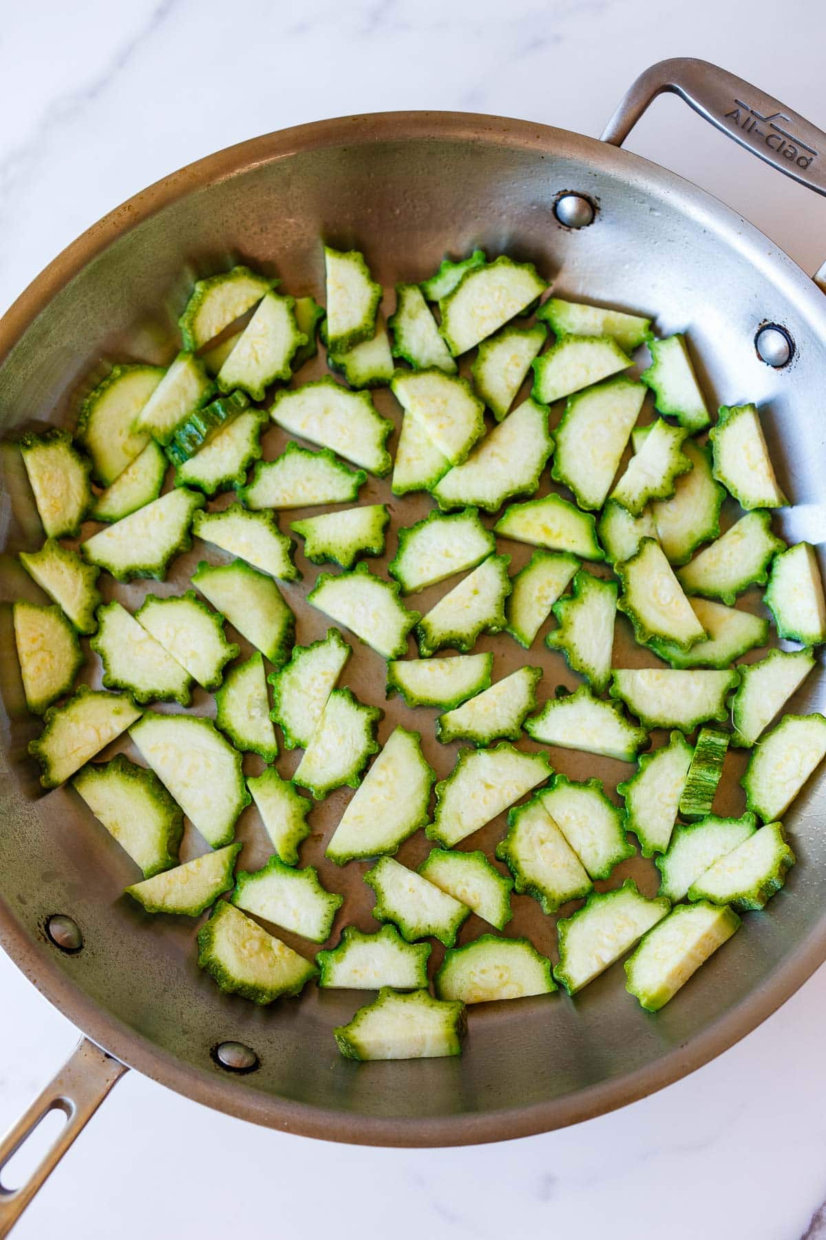 skillet with sliced half moon zucchini in an even layer.