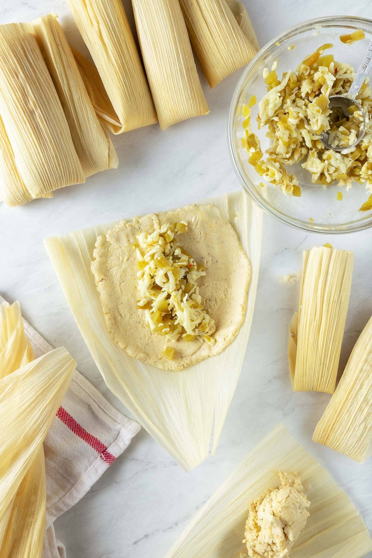 assembling tamales - an open corn husk with masa flour spread out and the cheese and chili filling down the center. 