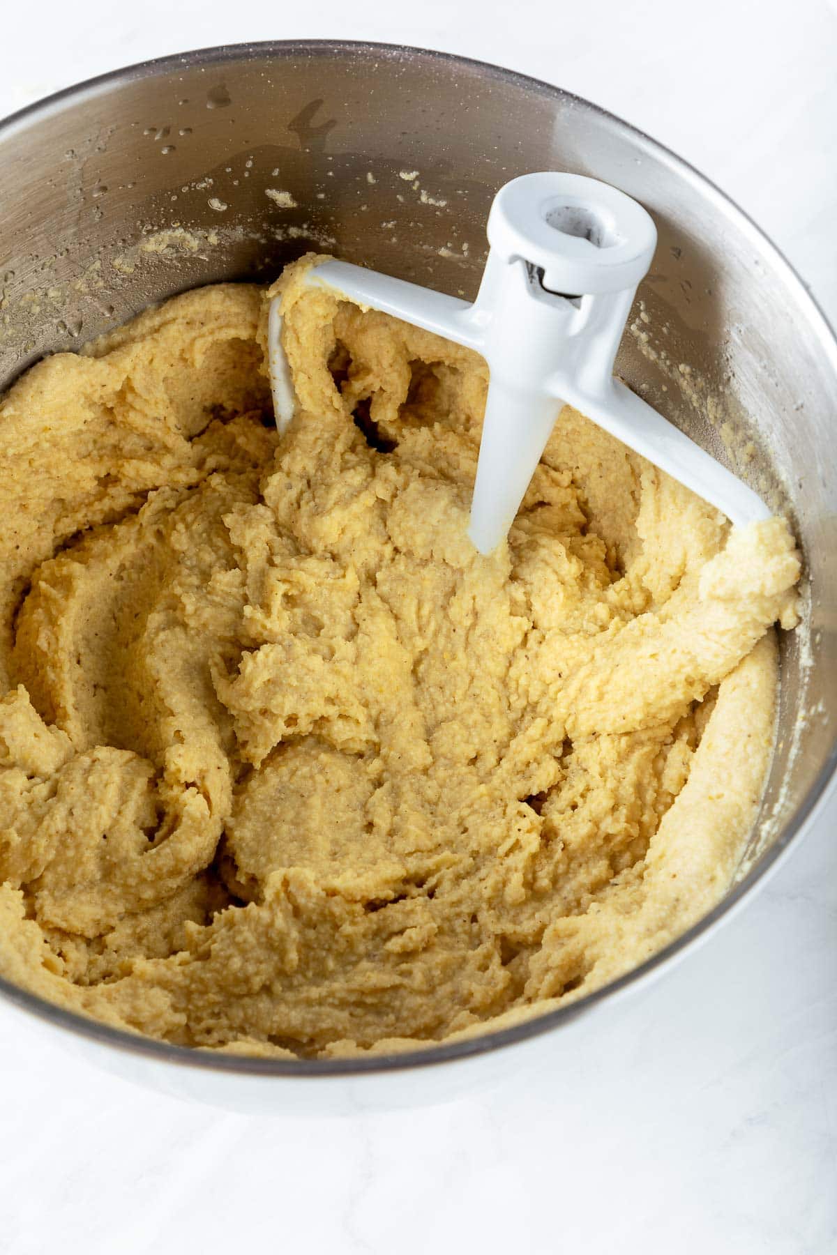 large metal mixing bowl with paddle attachment with prepared masa dough. 