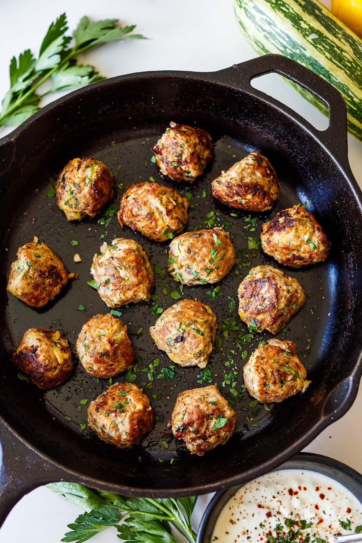 cast iron skillet with turkey and zucchini meatballs garnished with parsley.