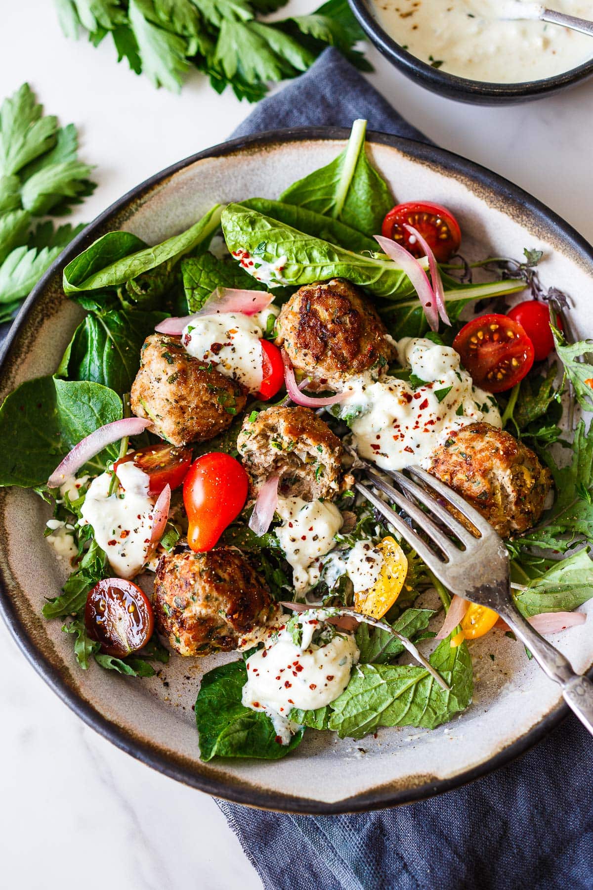 turkey and zucchini meatballs on bed of greens with cherry tomatoes, pickled onions, and feta yogurt dressing.