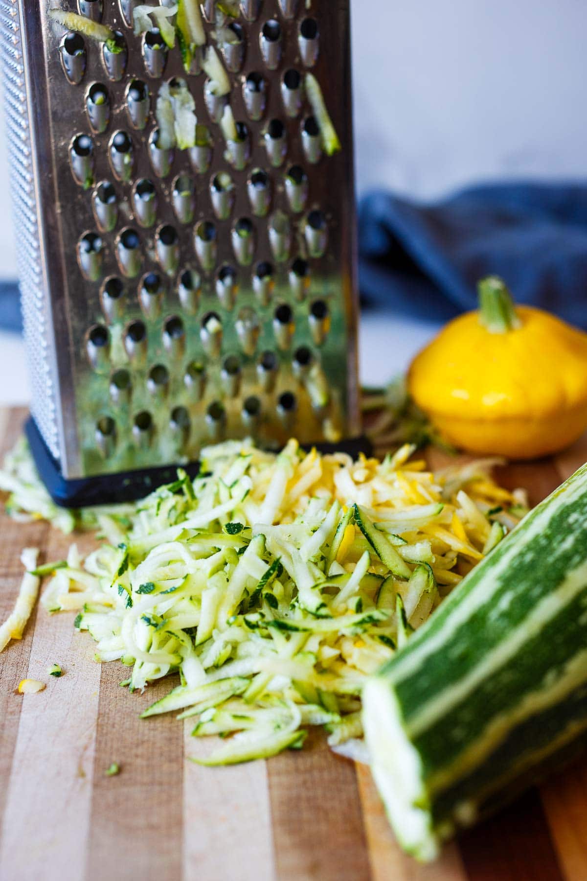 wood board with box grater and grated zucchini.