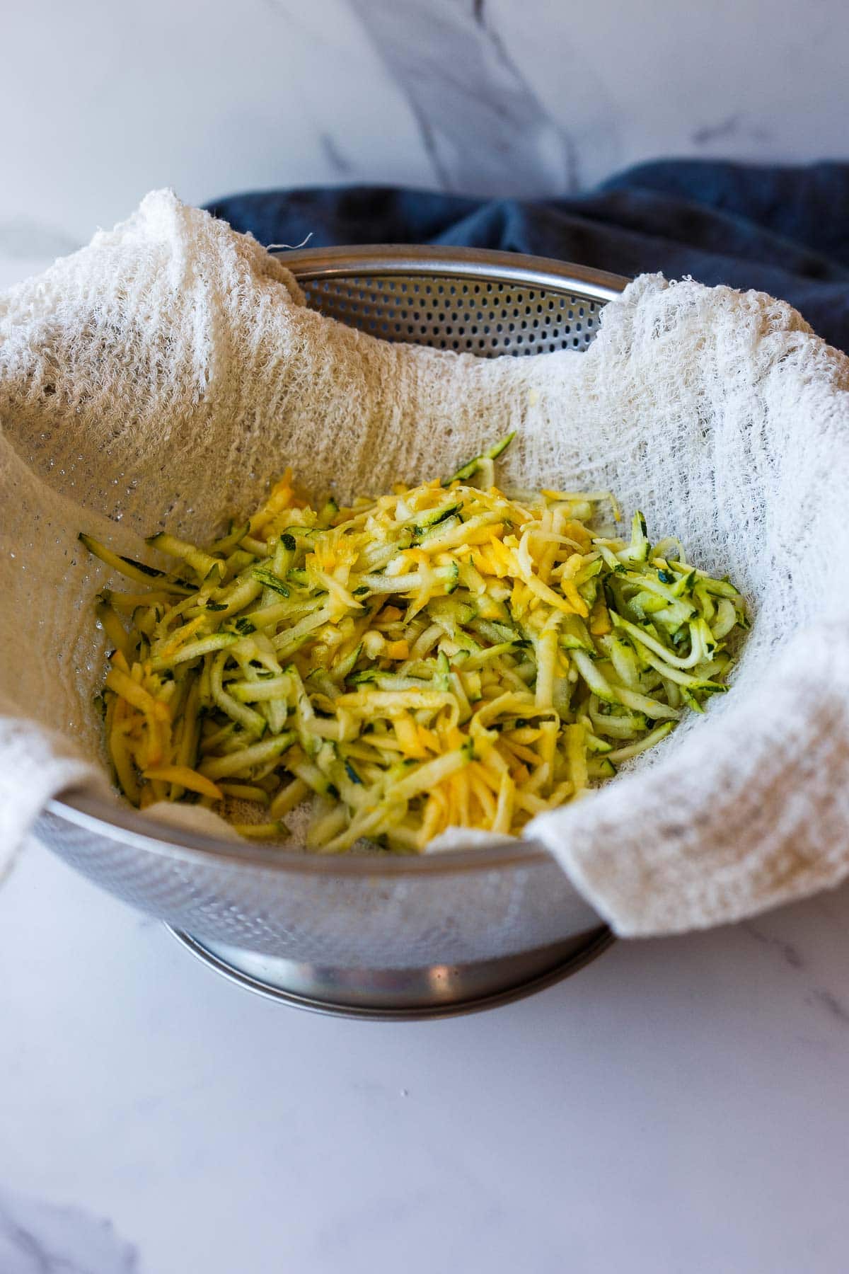 grated zucchini in cheesecloth in colander.
