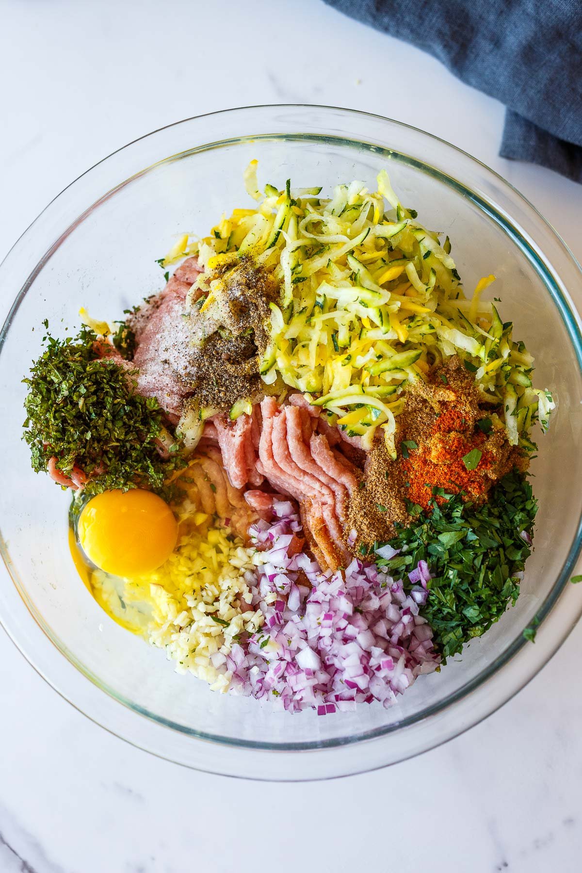 glass mixing bowl with ingredients for turkey zucchini meatballs before being mixed.