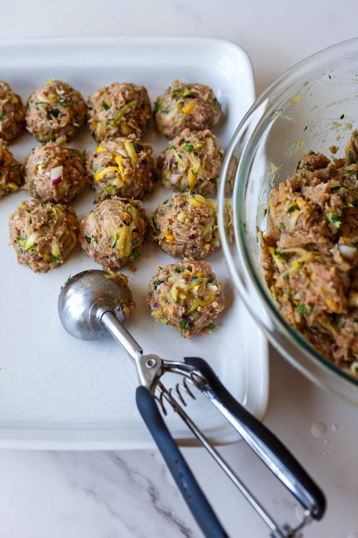 ice cream scoop forming turkey and zucchini meatballs and arranging on tray.