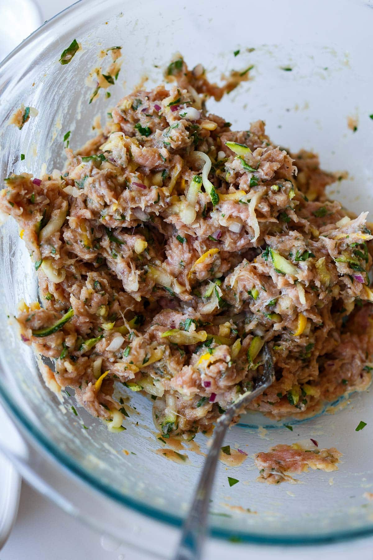 turkey zucchini meatball mixture mixed together in glass bowl with fork.