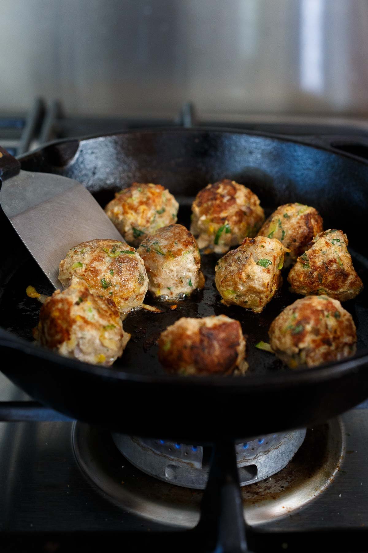 searing turkey and zucchini meatballs in cast iron skillet with metal spatula.