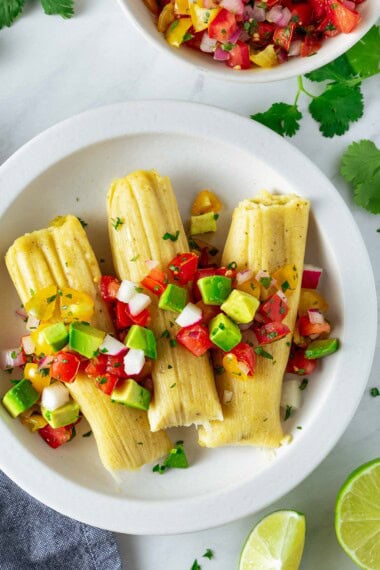 homemade tamales with salsa on a white plate.