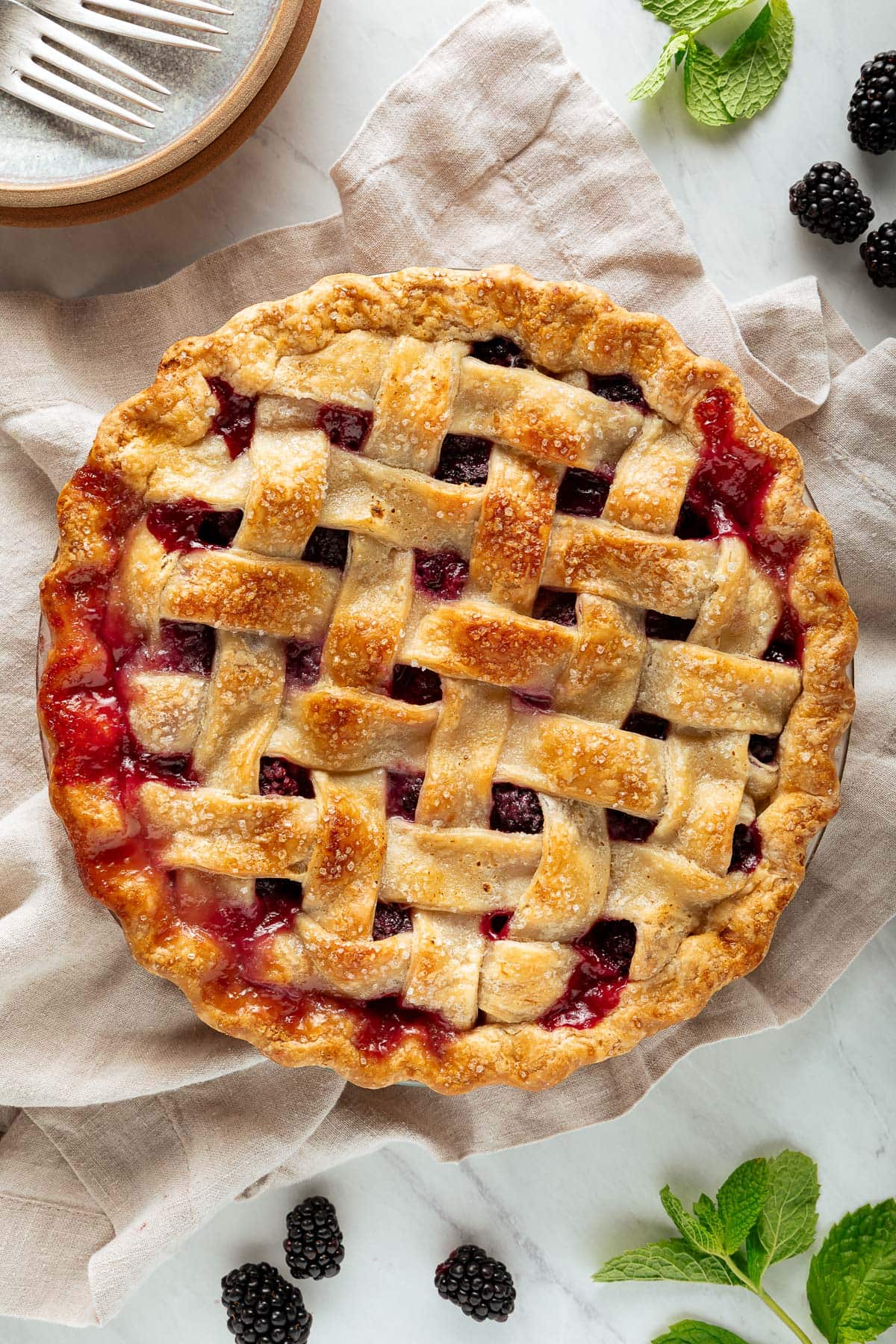 homemade blackberry pie baked with lattice crust, juices seeping through, with coarse sugar sprinkled over top.