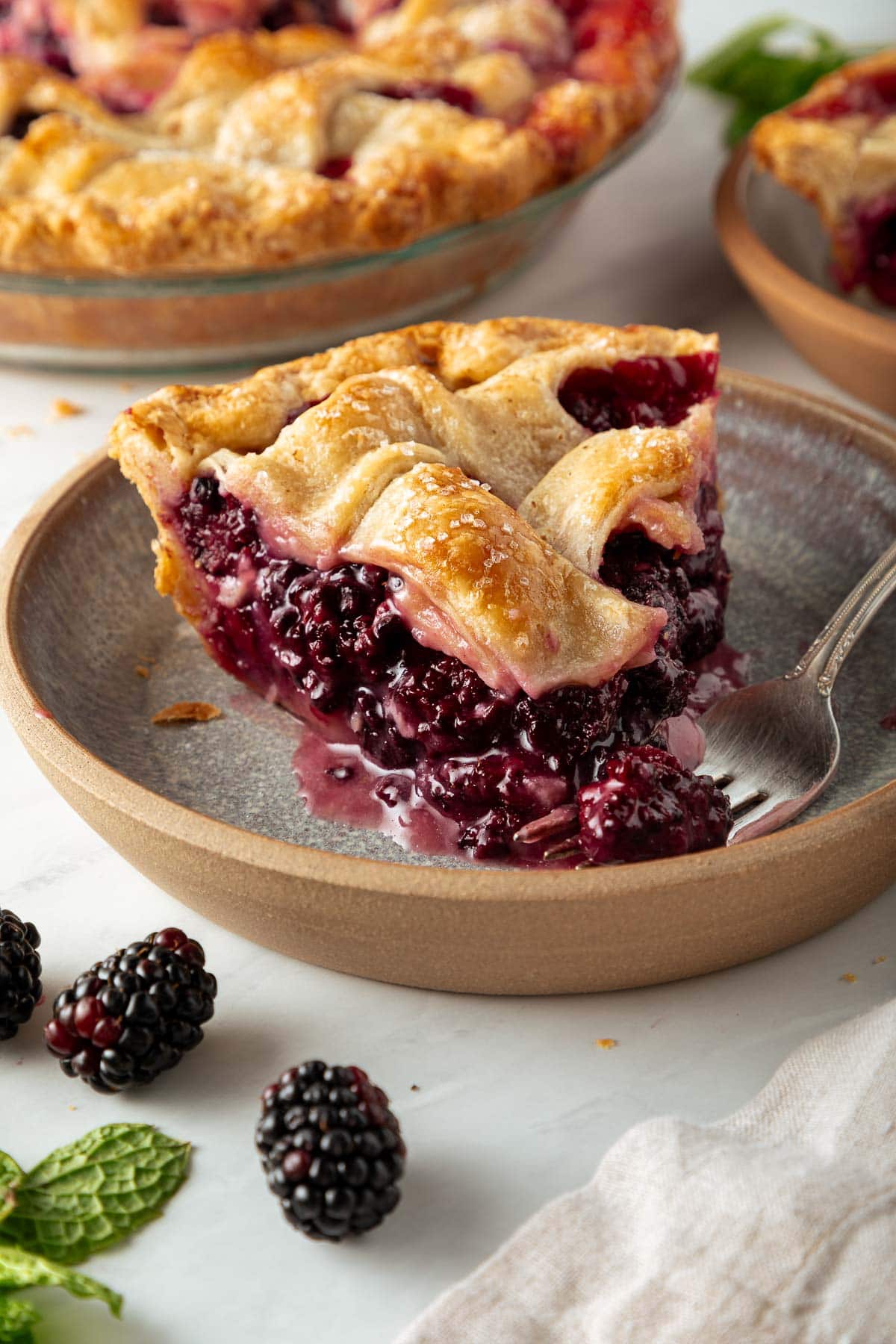 slice of blackberry pie on plate with juicy filling and a fork.