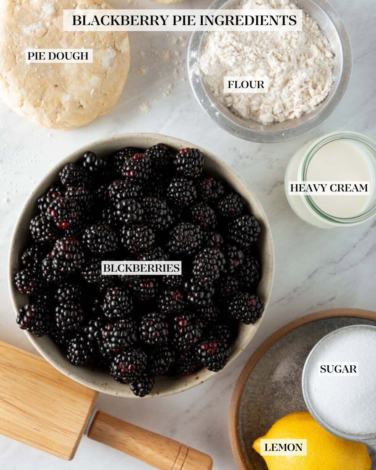 blackberry pie ingredients labeled and arranged neatly - pie dough, flour, heavy cream, blackberries, sugar, and lemon.