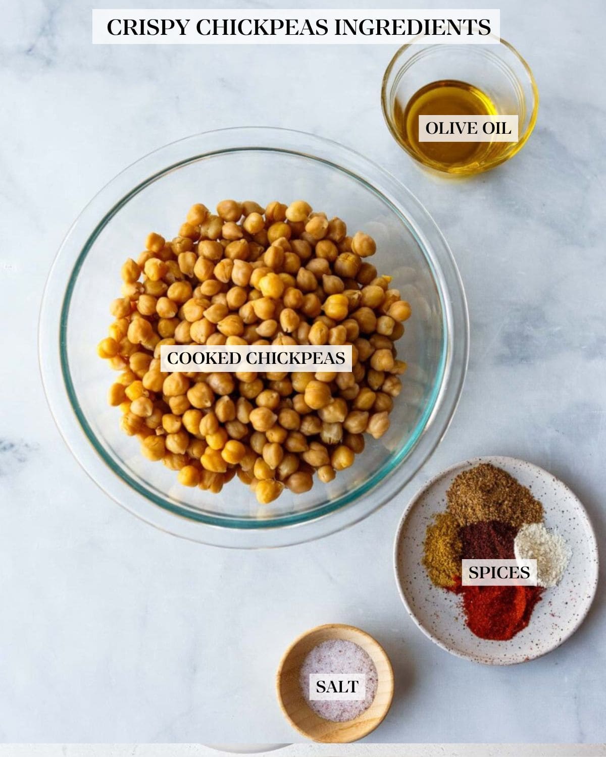 ingredients for making roasted chickpeas - glass bowl of olive oil, glass mixing bowl with cooked chickpeas, small dish with various spices, and tiny wood bowl with salt. 
