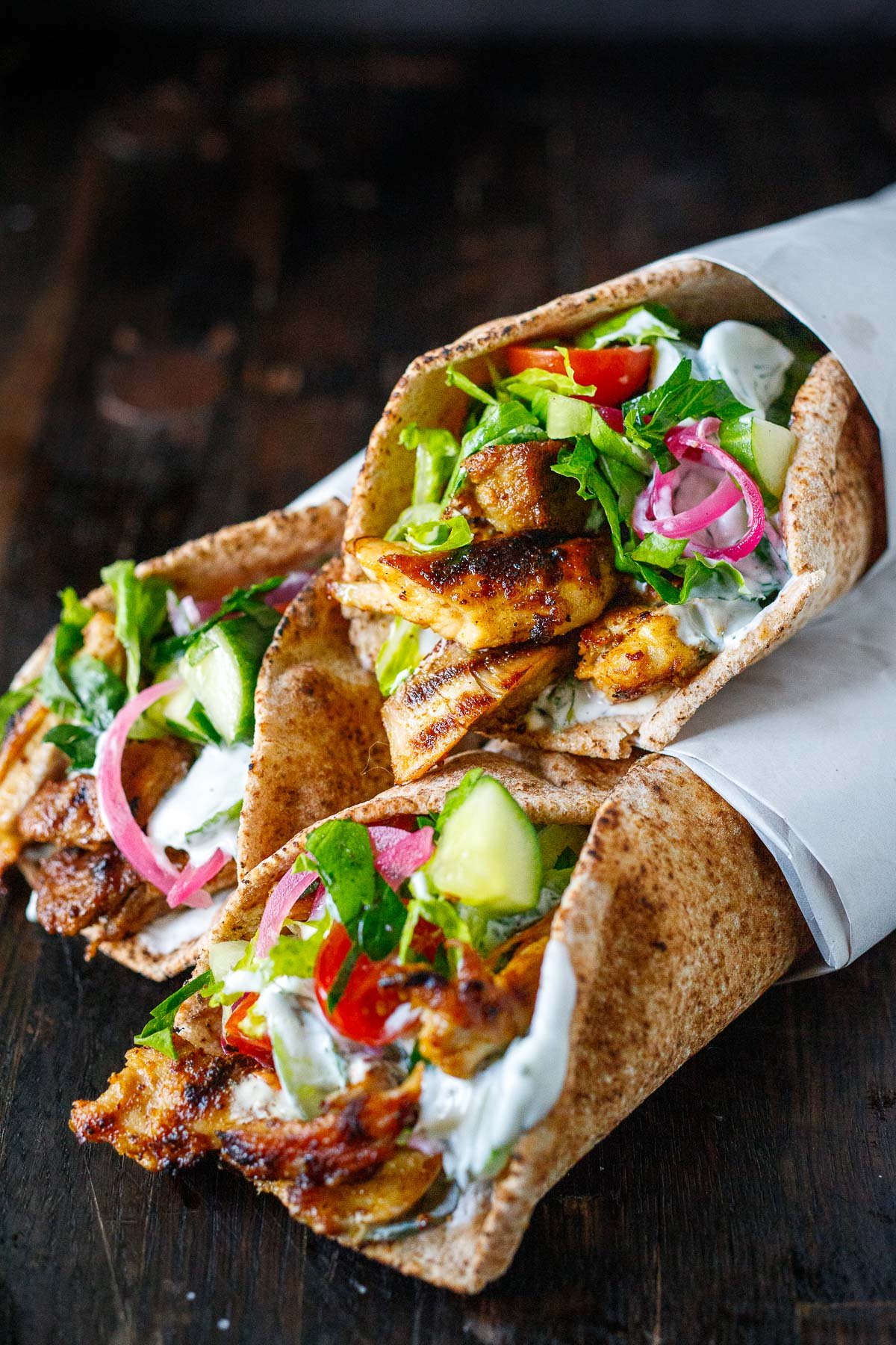 three chicken gyros in pita wrapped in paper, made with tzatziki sauce, tomato cucumber salad, and pickled onions. 