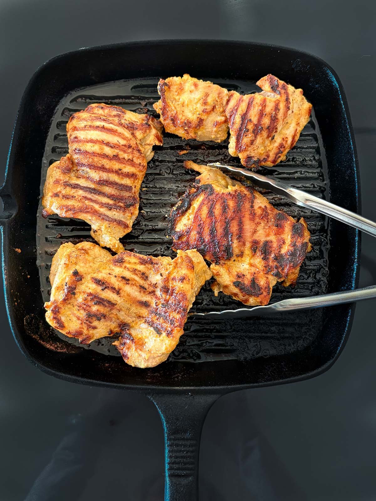 marinated chicken thighs on grill pan with grill marks with tongs. 
