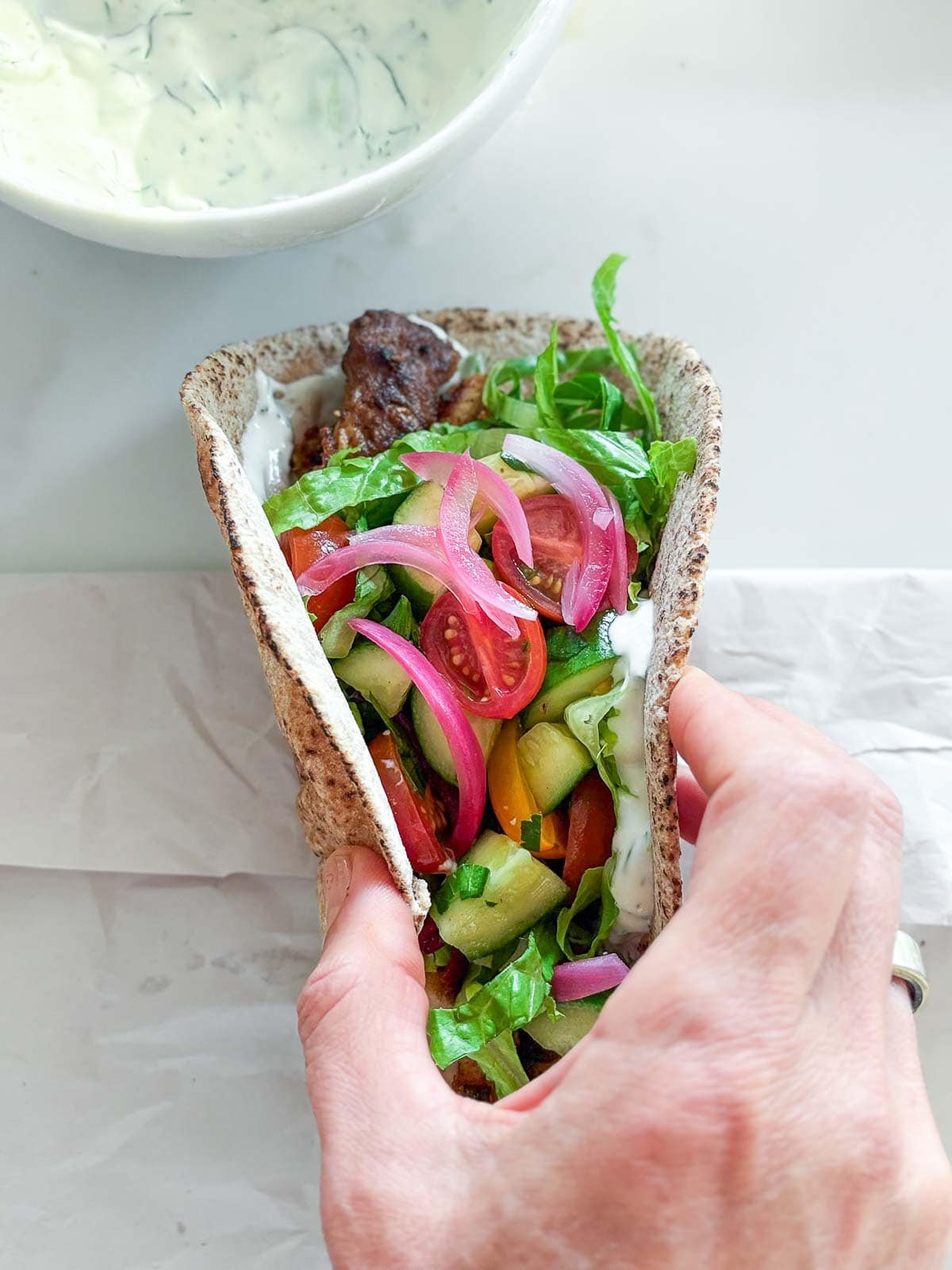 hand folding together the chicken gyro topped with pickled onions and tomato cucumber salad. 