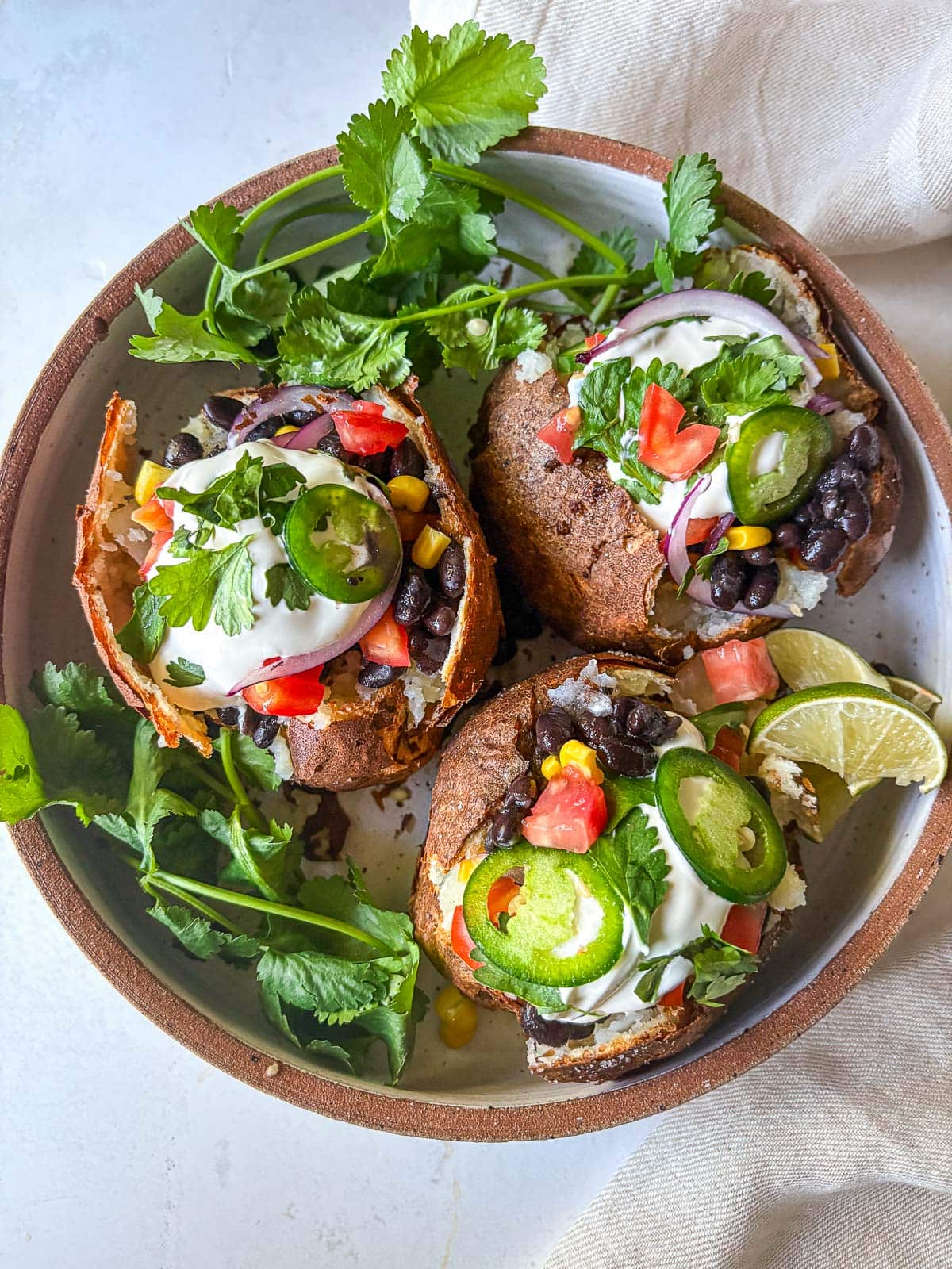 Mexican Baked Potatoes, stuffed with black beans and veggies topped with cilantro, jalapeno and sour cream.
