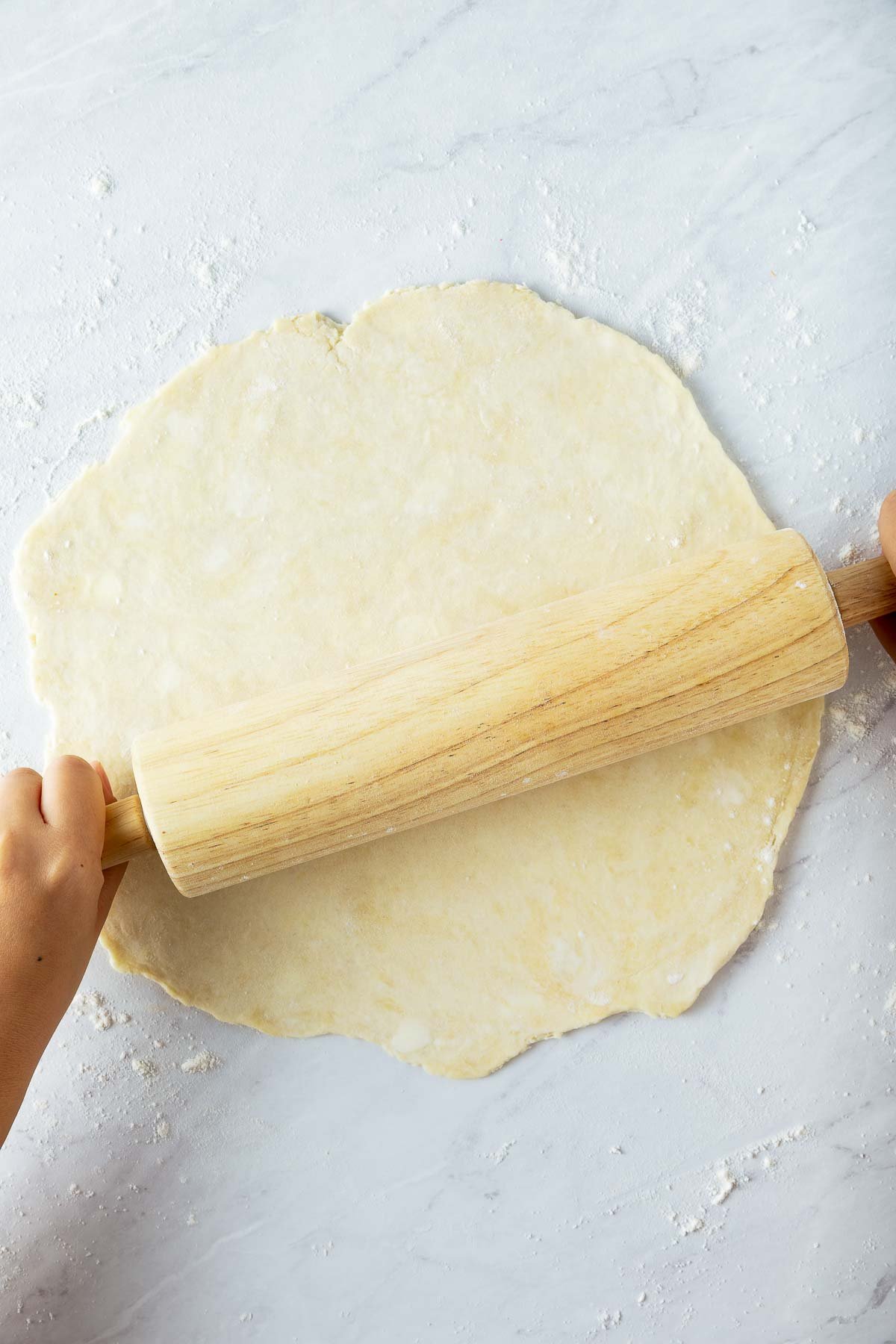 wood rolling pin rolling out pie dough into a circle. 