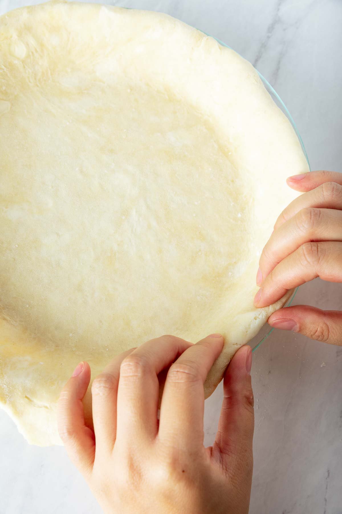hands crimping the edges of pie crust in a pie pan. 