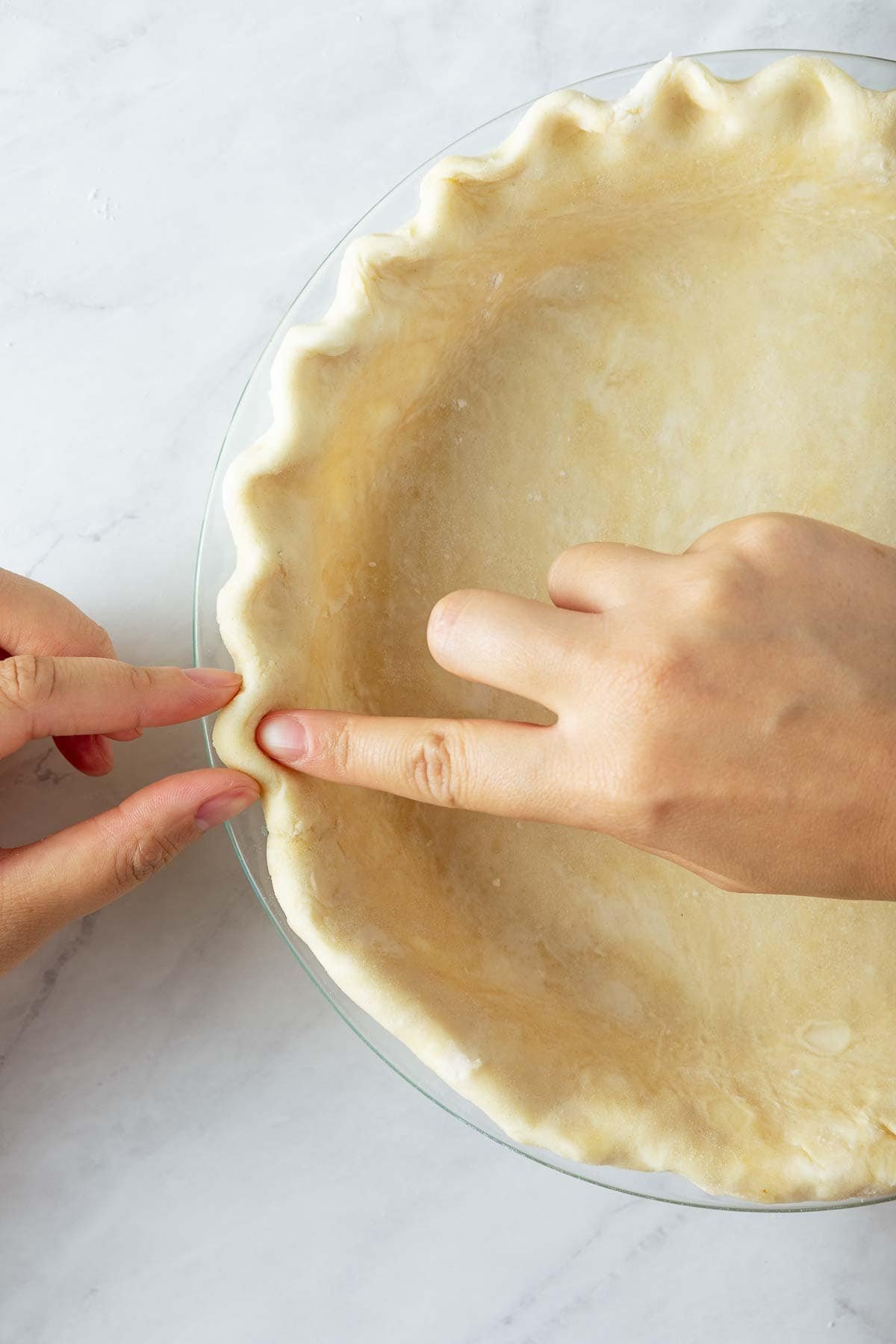 fingers crimping pie dough in a pie pan.
