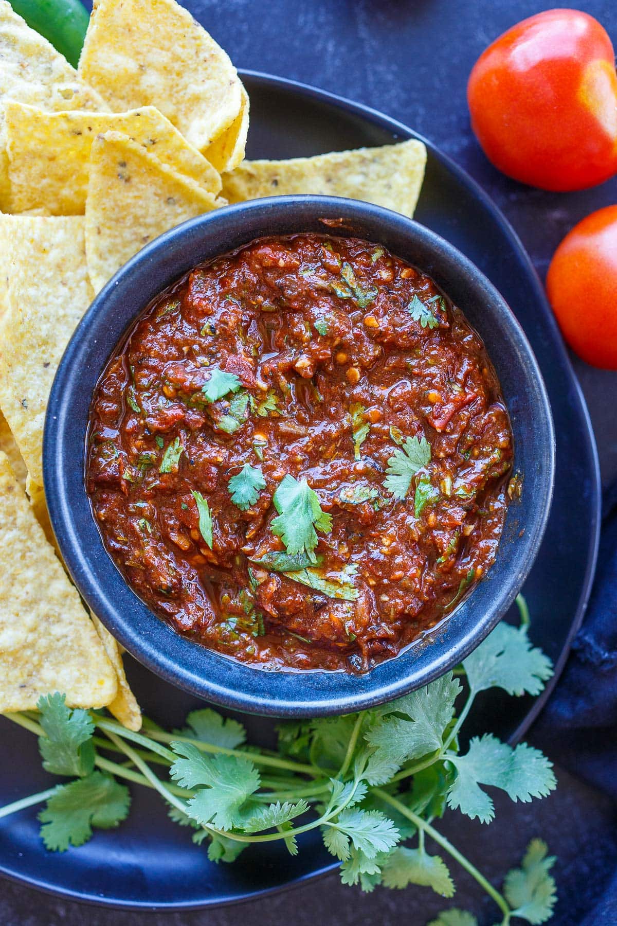 bowl of homemade salsa roja topped with cilantro on plate with tortilla chips.