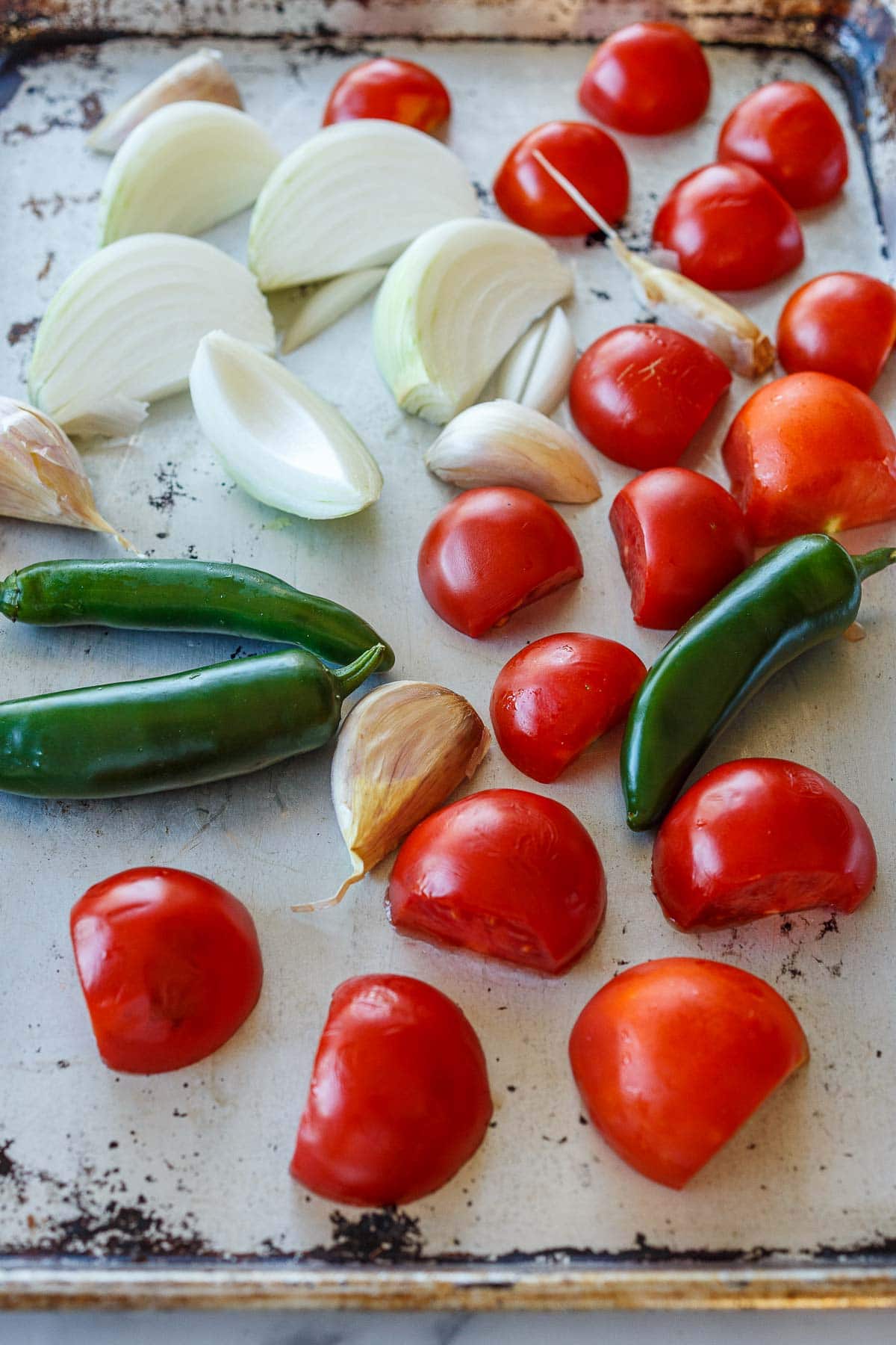 tomatoes, onions, garlic cloves in skin, and jalapeño and serrano peppers spread out on baking sheet. 