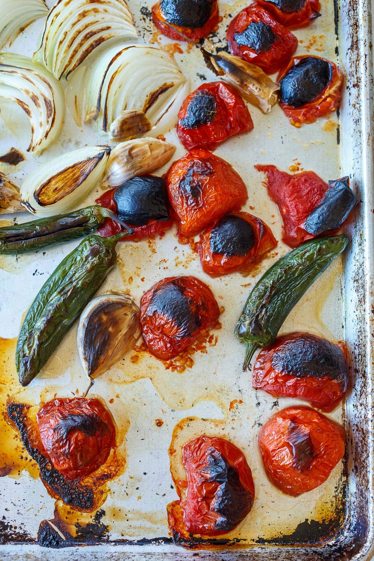 charred tomatoes, peppers, garlic, and onions on baking sheet.