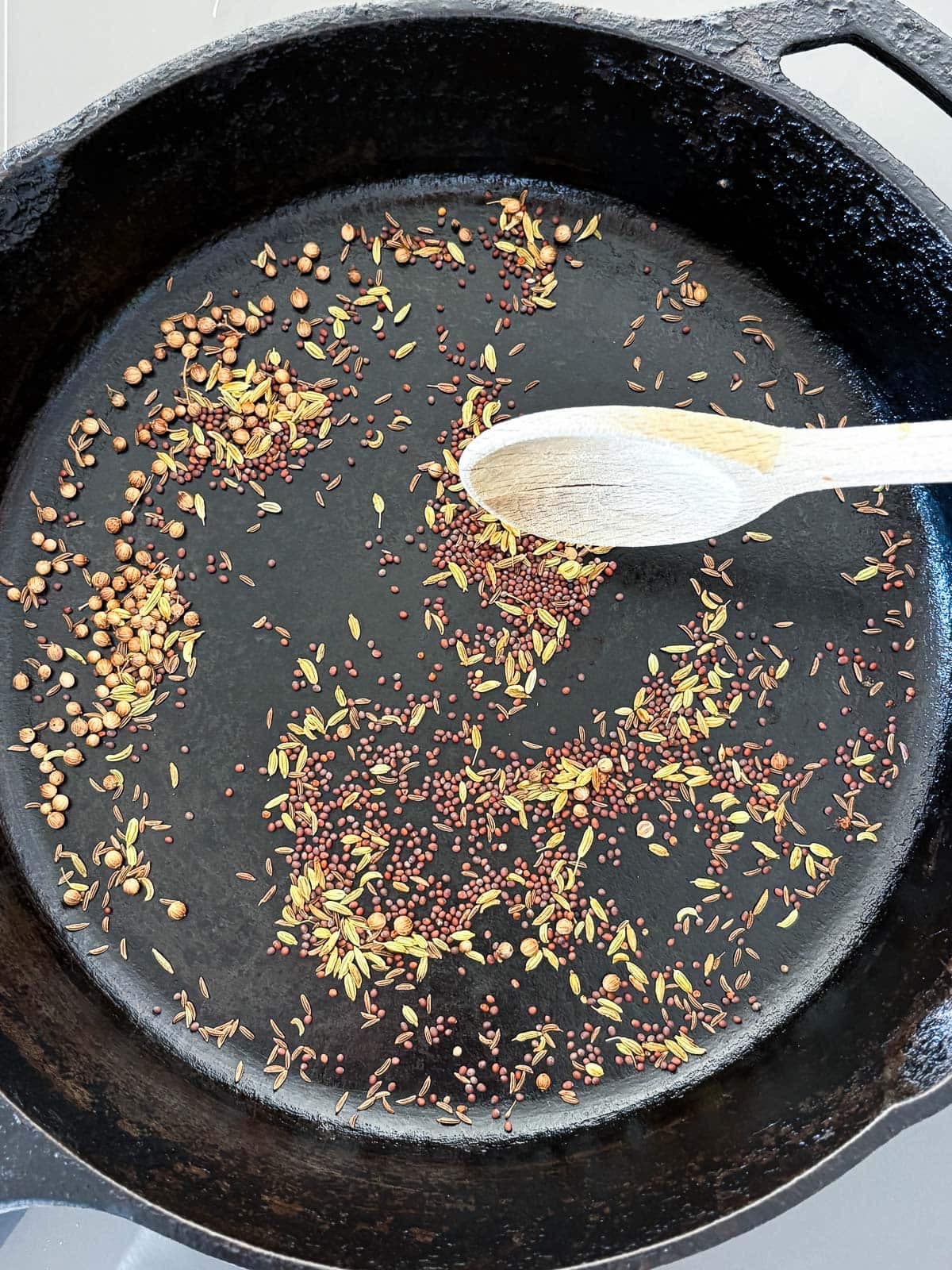 cast iron skillet with wood spoon stirring whole spices to toast them. 