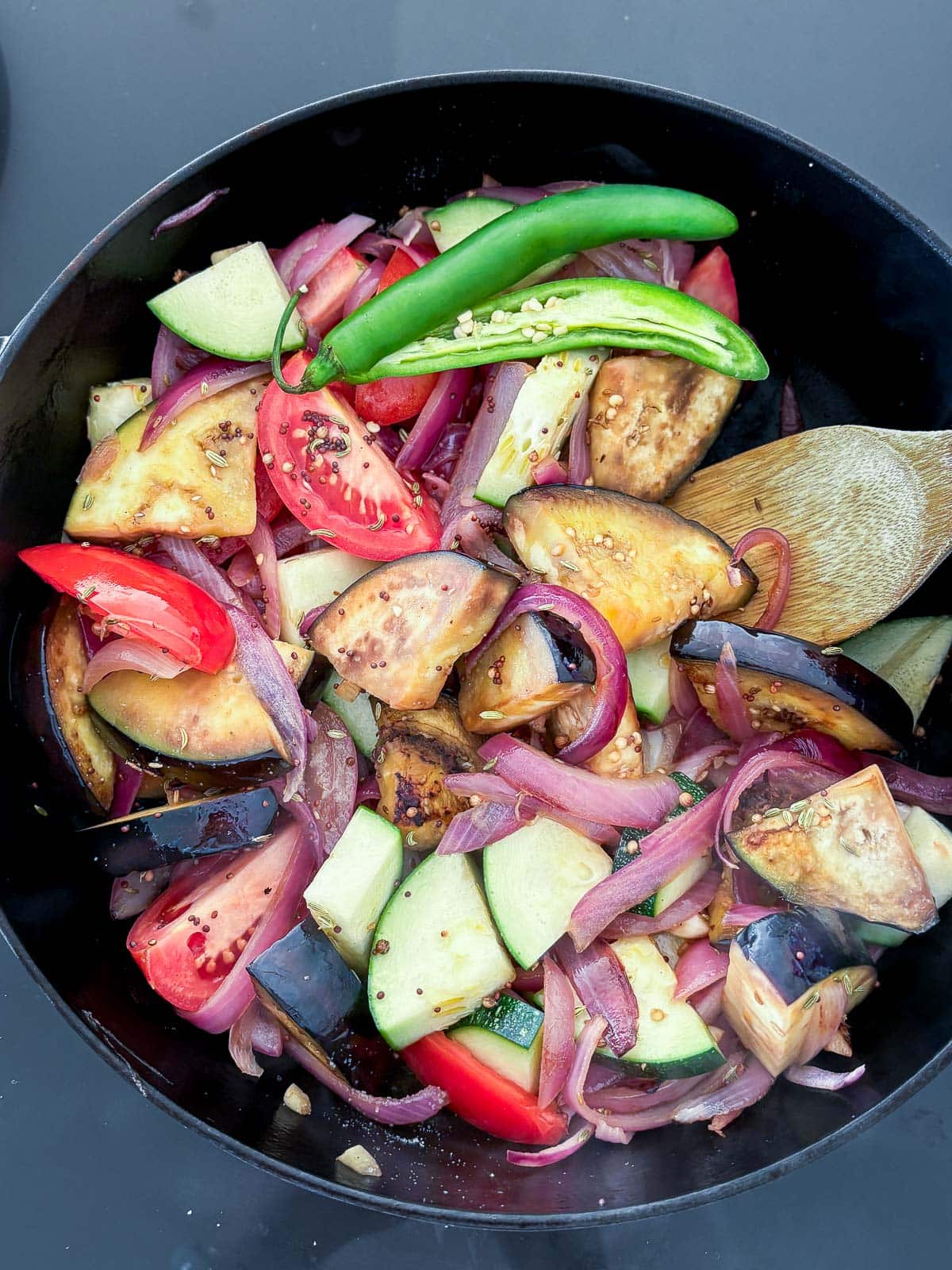 large pan with vegetables sautéing to make vegetable curry - tomatoes, eggplant, zucchini, chilies.