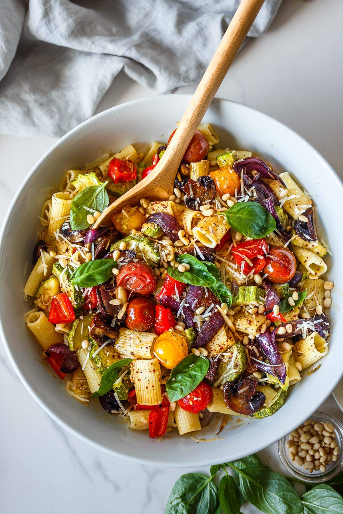 bowl of roasted vegetable pasta with pine nuts, parmesan, and basil. 