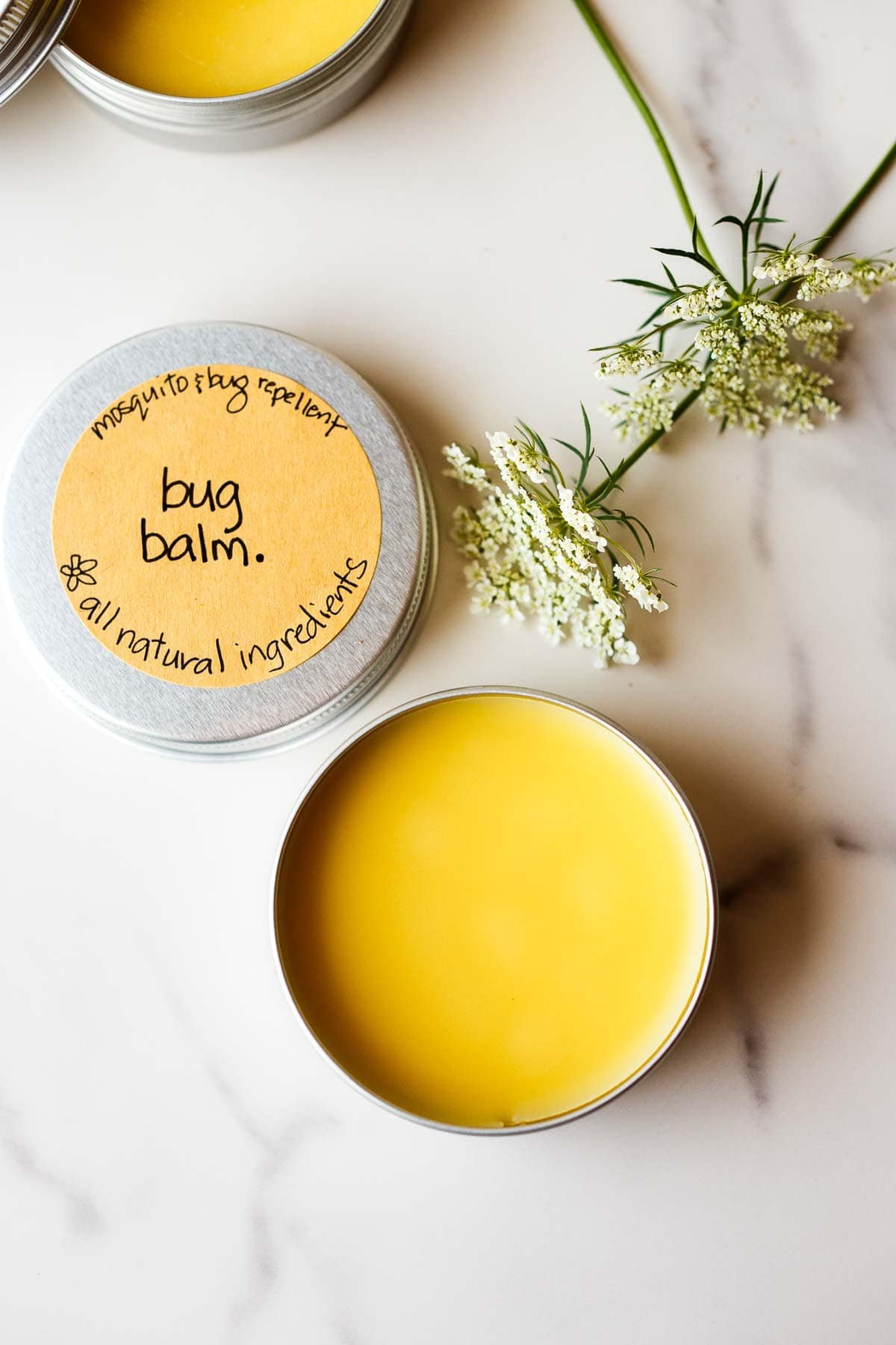 tin of solidified bug balm next to lid with brown label that says "mosquito & bug repellent bug balm all natural ingredients". 