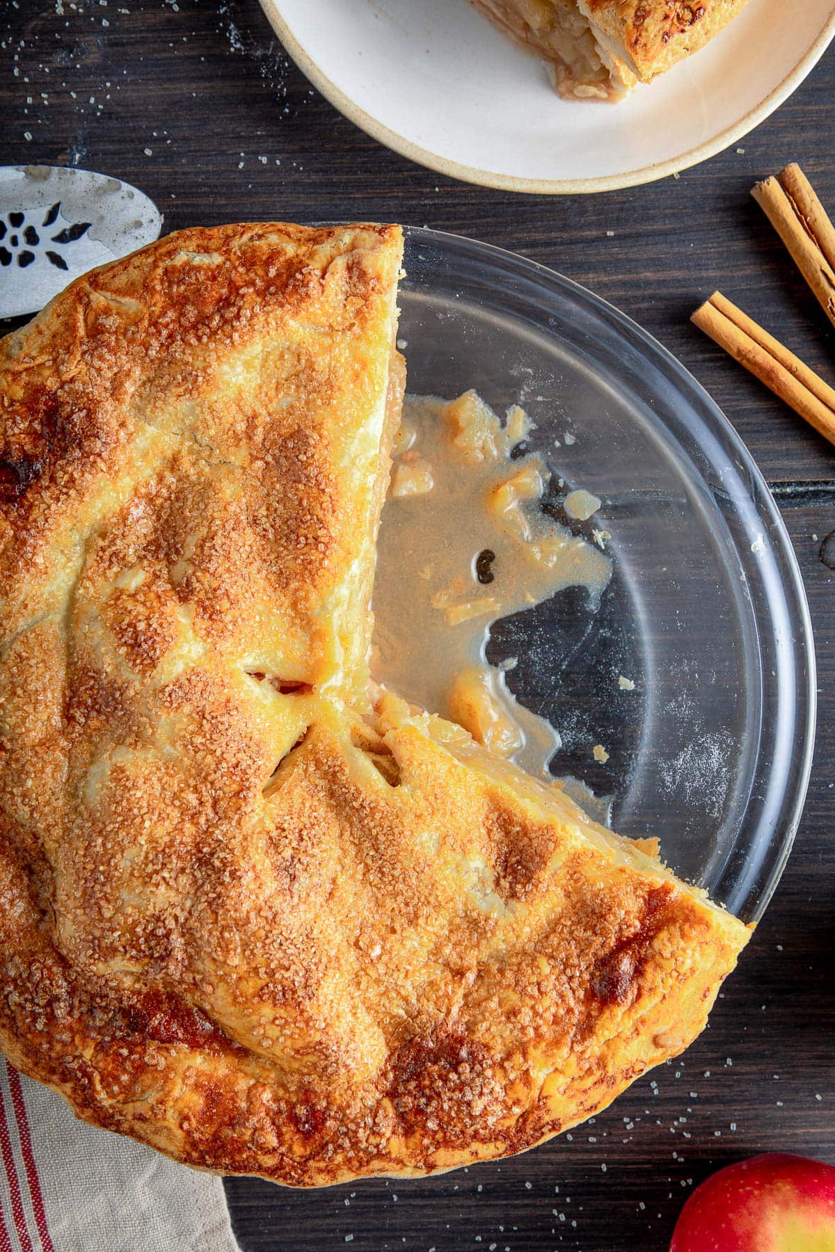glass pie dish with apple pie with coarse sugar topping, with a few slices removed from pan.
